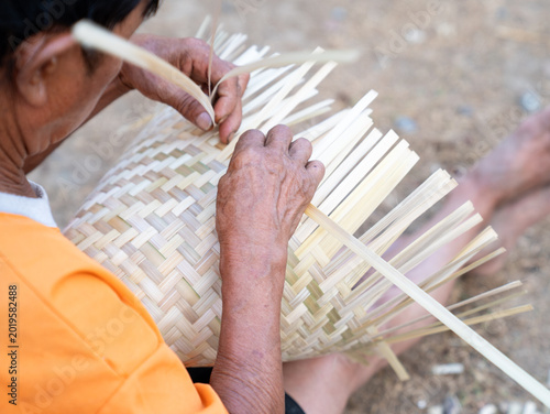 Fotografija Close up hands of a man weaving traditional pattern of house, this is Laos local wisdom handcrafted making basketry proceed by an old hand, basket rice cooker and bamboo plate make from bamboo