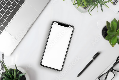 Flat lay overhead view of a modern smartphone with an empty white screen on a bright desk background featuring a laptop, black pen, eyeglasses, and green plants, ideal for mobile app design mockups.