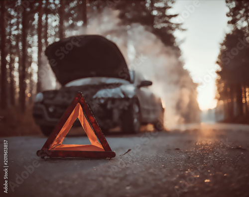 Broken down car on a forest road with smoke and hazard triangle
