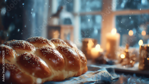 A braided, golden loaf sits by a window with snowy, candlelit, festive ambiance