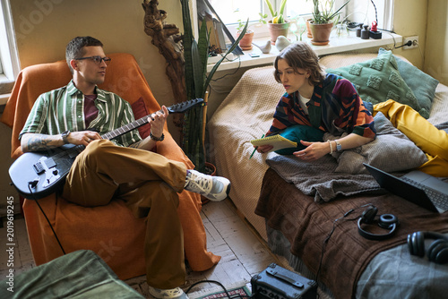 Foto Young adult man playing electric guitar while young adult woman taking notes in