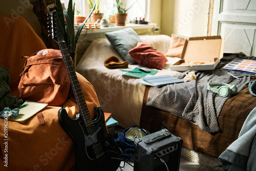Quadro su tela Wide shot of teenager bedroom showing guitar, amplifier, headphones, notebooks, backpack, and pizza box, suggesting creative student lifestyle