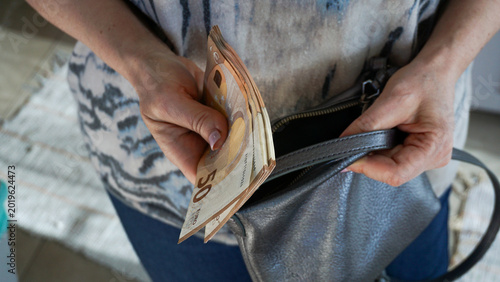 Bild auf Leinwand Woman placing euro banknotes into small handbag representing personal finance, s