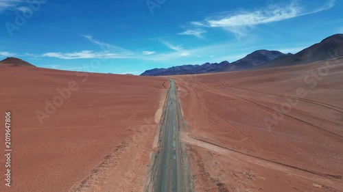 Ascending drone shot revealing two motorbikes riding on empty desert road through vast arid landscape with volcanic mountains and vivid blue sky