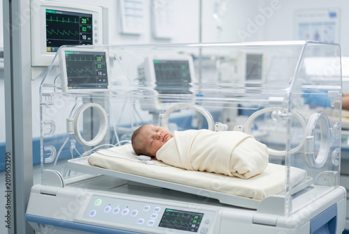 Newborn baby sleeping peacefully inside medical incubator at hospital ward