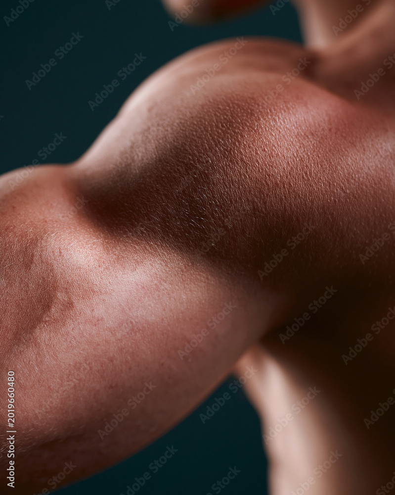 Fototapeta premium Strong arm muscles flex under soft lighting. Toned skin glistens with subtle shine. Background fades into deep, dark tone. Focus on power and physical strength. Ideal for fitness, health