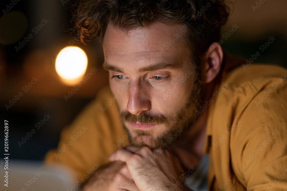 Fototapeta premium Man rests fingers near tablet screen. Focused gaze suggests deep thought or concentration. Soft lighting highlights his calm, contemplative expression. Ideal for scenes of study, planning