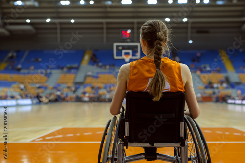 Rear view of a female athlete in a wheelchair facing a basketball hoop in an indoor arena