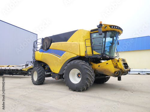 A yellow combine harvester is parked before heading out into the field to harvest crops. The header and mower are removed.
