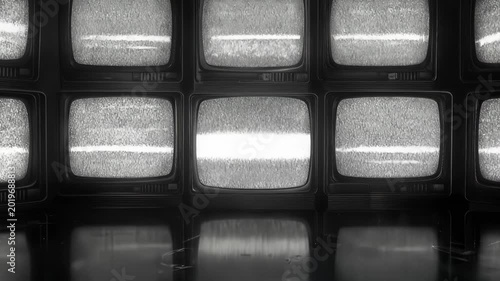 Retro television wall displaying static and white noise. Vintage analog screens with flickering interference in dark room. Lockdown wide shot.