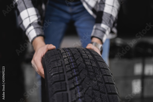 Close-up of male adult handling winter car tire in workshop setting