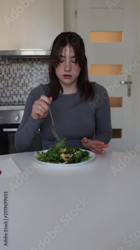 Vertical screen woman refuses sweets and forces herself to eat healthy salad while preparing body for summer weight loss and disciplined nutrition routine