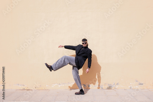 A daring man poses in front of a peach-colored wall
