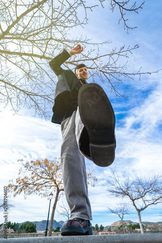 A low-angle shot of a young man kicking the camera in an outdoor park