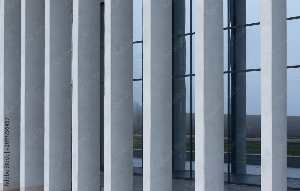 Fototapeta premium Modern building facade with tall vertical columns and glass windows. Minimalist architecture with gray exterior lines and reflective surfaces. Ideal