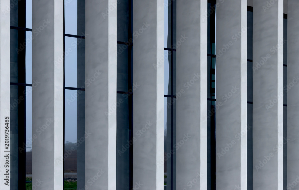 Fototapeta premium Modern building facade with vertical concrete fins and dark window panels. Geometric exterior lines create a clean architectural pattern. Suitable for