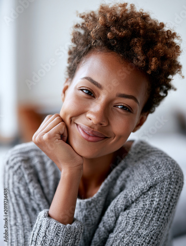 Portrait of a beautiful young Black woman with short curly hair resting her chin on hand with a serene smile.