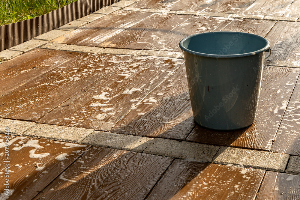 Naklejka premium Washing the paving slabs on the terrace in front of the house in the garden, a bucket with hot water and detergent, water with detergent spilled on the tiles to remove dirt from the tiles,