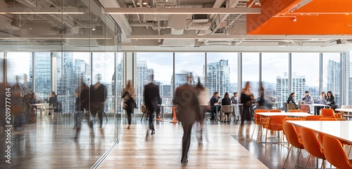 Bright and modern office space with employees walking and working by large glass windows overlooking city skylines