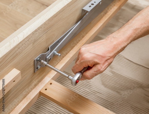 Hand tightening a ratchet wrench on wooden furniture. DIY assembly for joinery, repair, and home improvement. Close up of tool use on timber frame hardware..