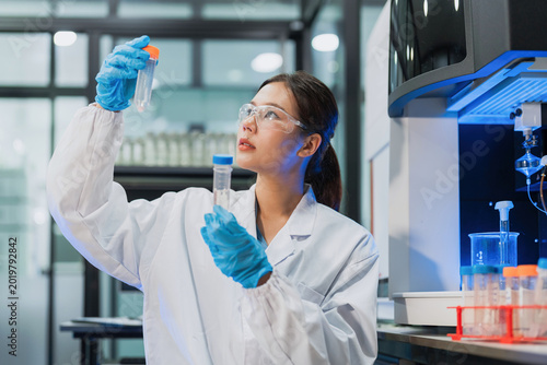 Photography Asian female scientist holding and comparing two sample tubes for clinical testing in lab