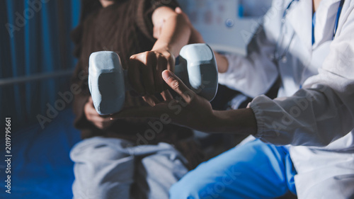 Old woman training with physiotherapist using dumbbells at home. Therapist assisting senior woman with exercises in nursing home. Elderly patient using dumbbells with outstretched arms.