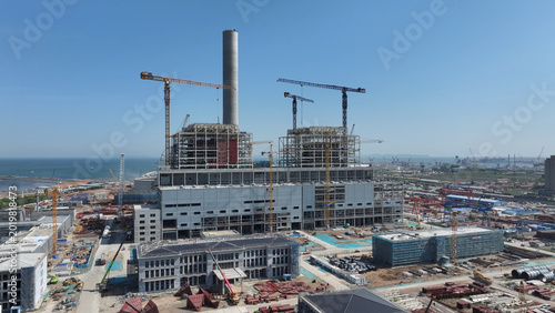 Foto Coastal thermal power plant under construction with cranes and smokestack on cle