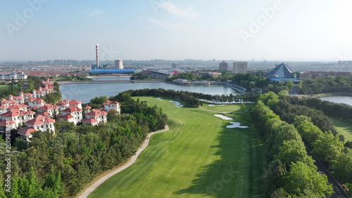 Bild auf Leinwand Golf course with lakeside villas and industrial area in the distance under clear