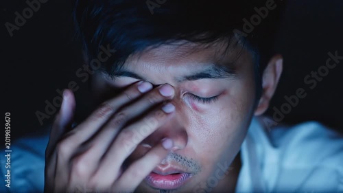 close-up of a tired young man rubbing his forehead, looking tired in front of the computer.