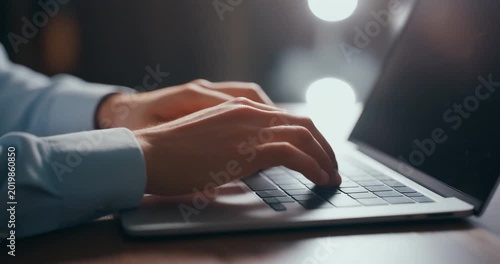 Business professional typing on laptop keyboard at office desk during night time.