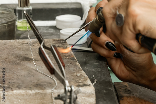 Quadro em tela Jeweler using a torch to solder a delicate chain on a workbench
