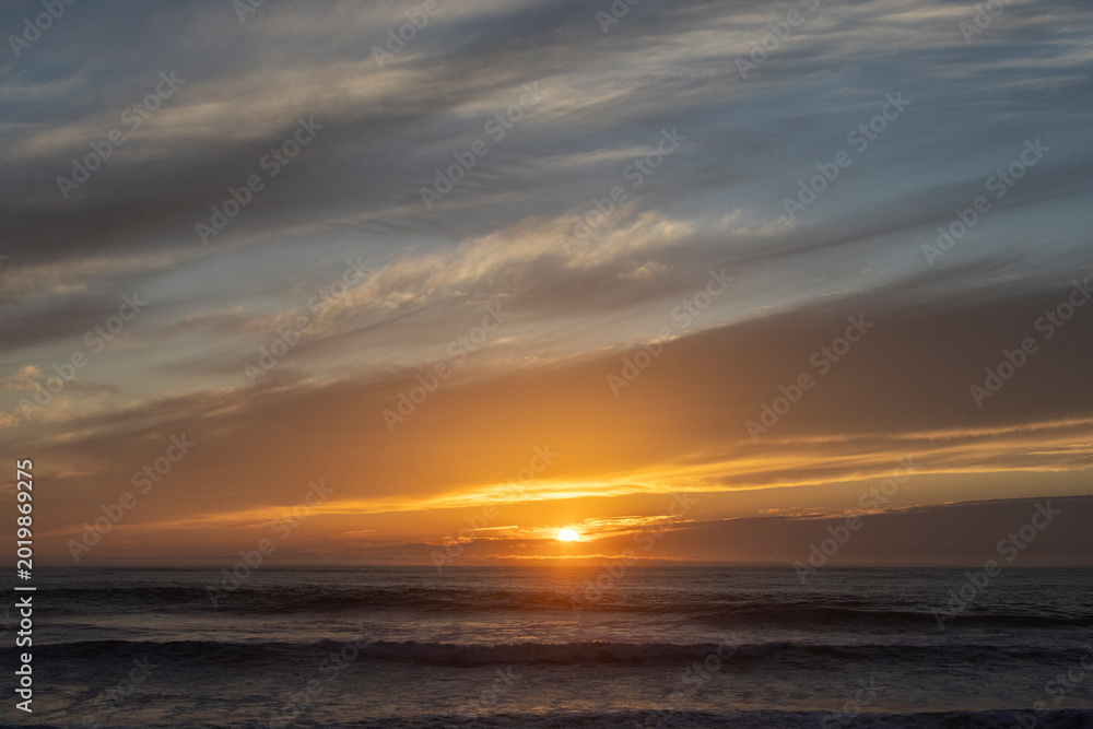 Obraz premium Golden sunset over the ocean with dramatic clouds and gentle waves
