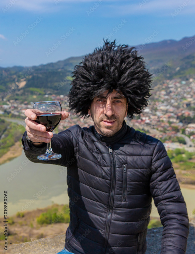 Obraz premium Georgian man in a papakhi with a glass of wine. Selective focus.