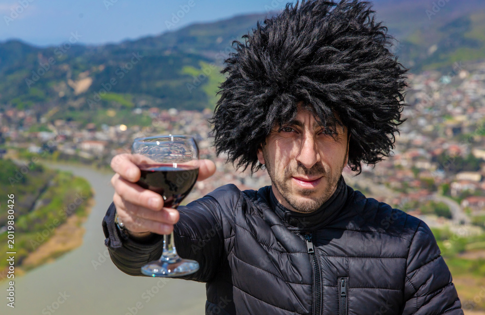 Obraz premium Georgian man in a papakhi with a glass of wine. Selective focus.