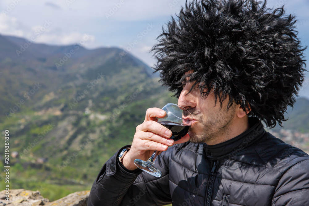 Fototapeta premium Georgian man in a papakhi with a glass of wine. Selective focus.