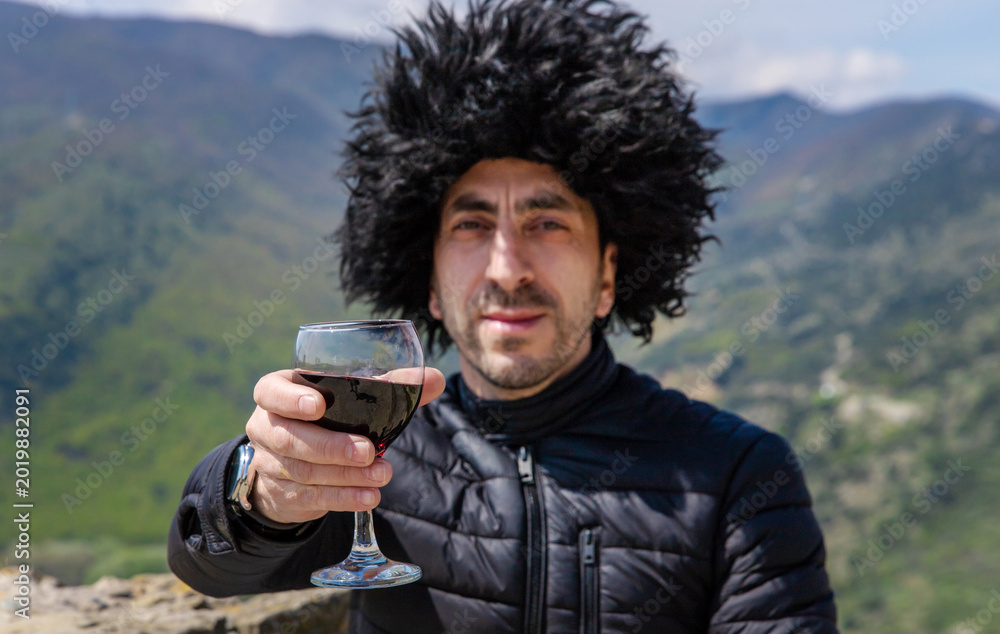 Fototapeta premium Georgian man in a papakhi with a glass of wine. Selective focus.