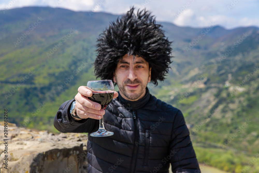 Obraz premium Georgian man in a papakhi with a glass of wine. Selective focus.