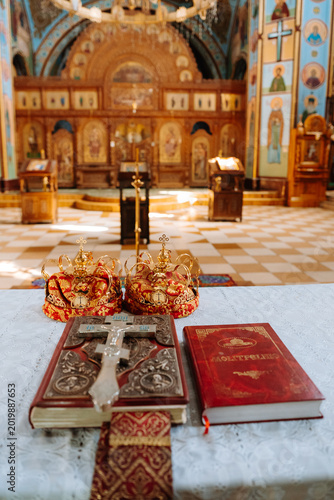 Foto Orthodox wedding ceremony attributes in church interior: golden crowns, holy bible with cross, and prayer book on altar table