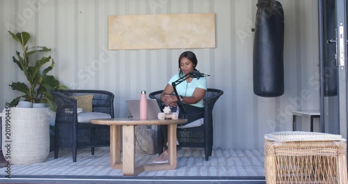 African American woman on patio checking laptop and starting podcast, speaking into boom mic