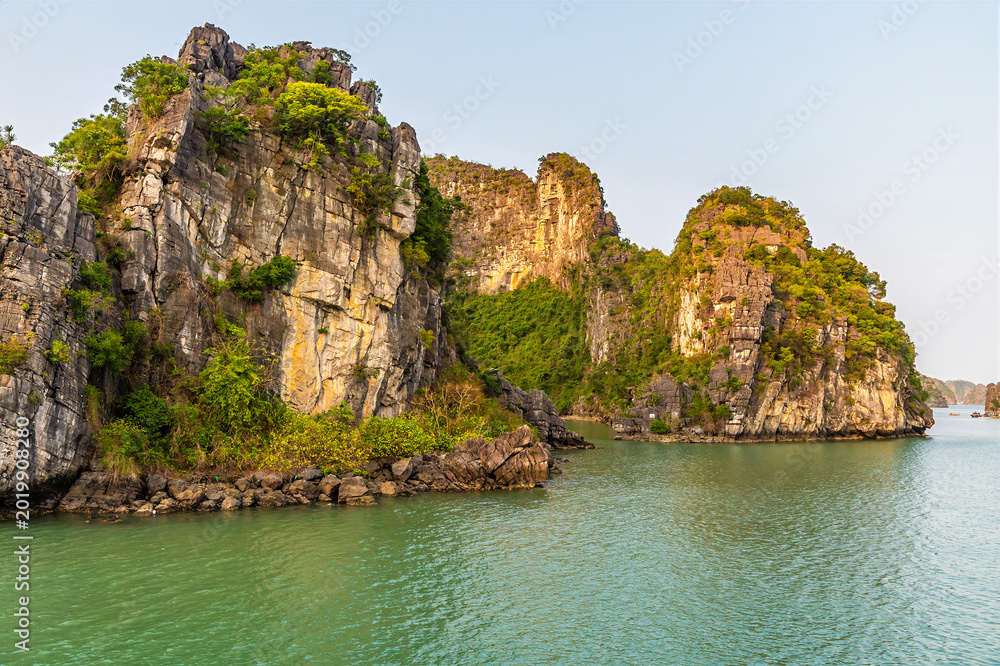 Fototapeta premium A view from a cruise ship into a lagoon surrounded by Karst limestone cliffs in Ha Long Bay, Vietnam illuminated by the evening light