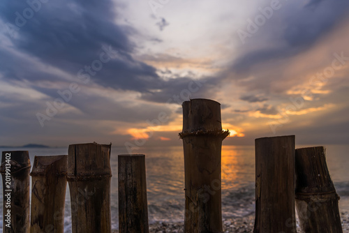 Foto Sunset Silhouette: Wooden posts stand resolute against a breathtaking seascape, silhouetted by the vibrant hues of the setting sun, where the sky and sea blend in a tranquil embrace
