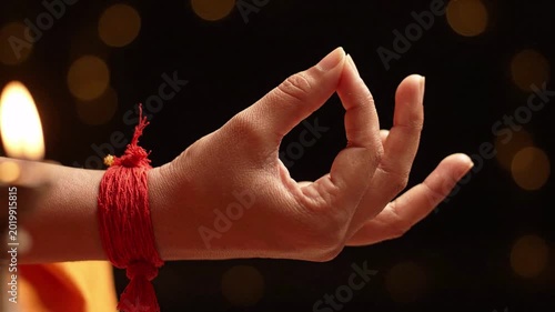 Close-up of a hand performing a mudra gesture with a red thread tied around the wrist, soft bokeh lights in the background, suggesting meditation and spirituality