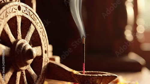 Incense stick burning in clay lamp with wooden wheel and smoke rising, spiritual atmosphere, cultural tradition, soft light