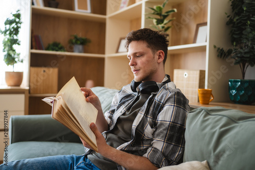 Konstfotografi Young man reading book on sofa at home
