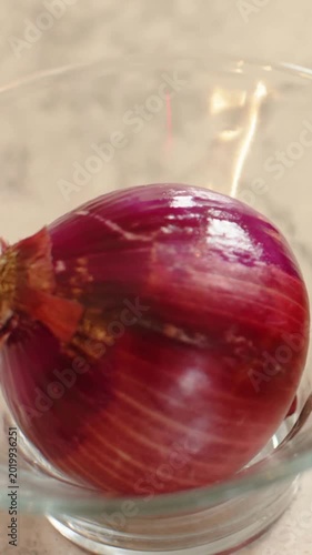 Vertical video: Rising camera showing red onion in glass bowl on marble counter, showing backsplash