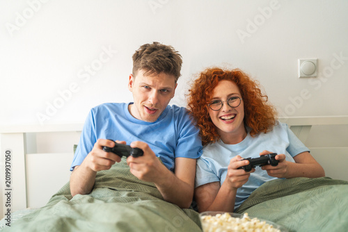 Couple playing video games in bed feeling bored