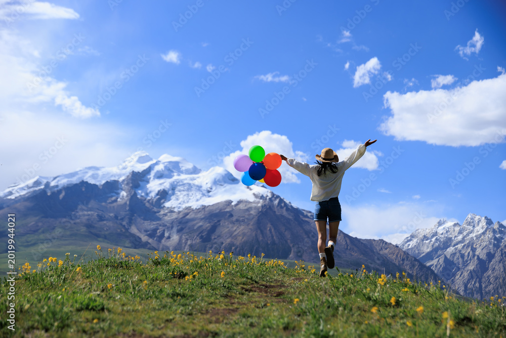 Obraz premium Woman with colored balloons on sunset grassland mountain top