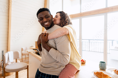 Foto Happy interracial couple hugging and kissing in kitchen