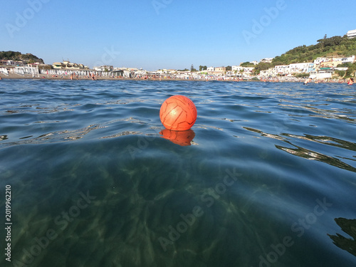 Tableau sur toile Orange water polo ball floating on crystal clear Mediterranean surface at eye-le