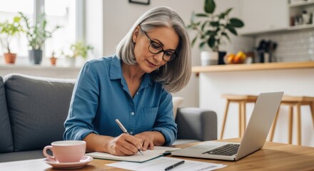 Focused Mature Woman Working from Home, Writing in Notebook with Lapto